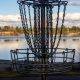 Disc golf basket on pretty park course near a lake under blue sk