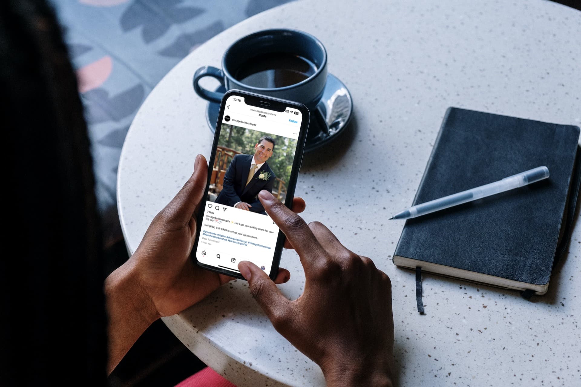 african american iPhone 11 in the hands of an African-American man beside the cup of coffee and notebook looking at a barbershop post on instagram