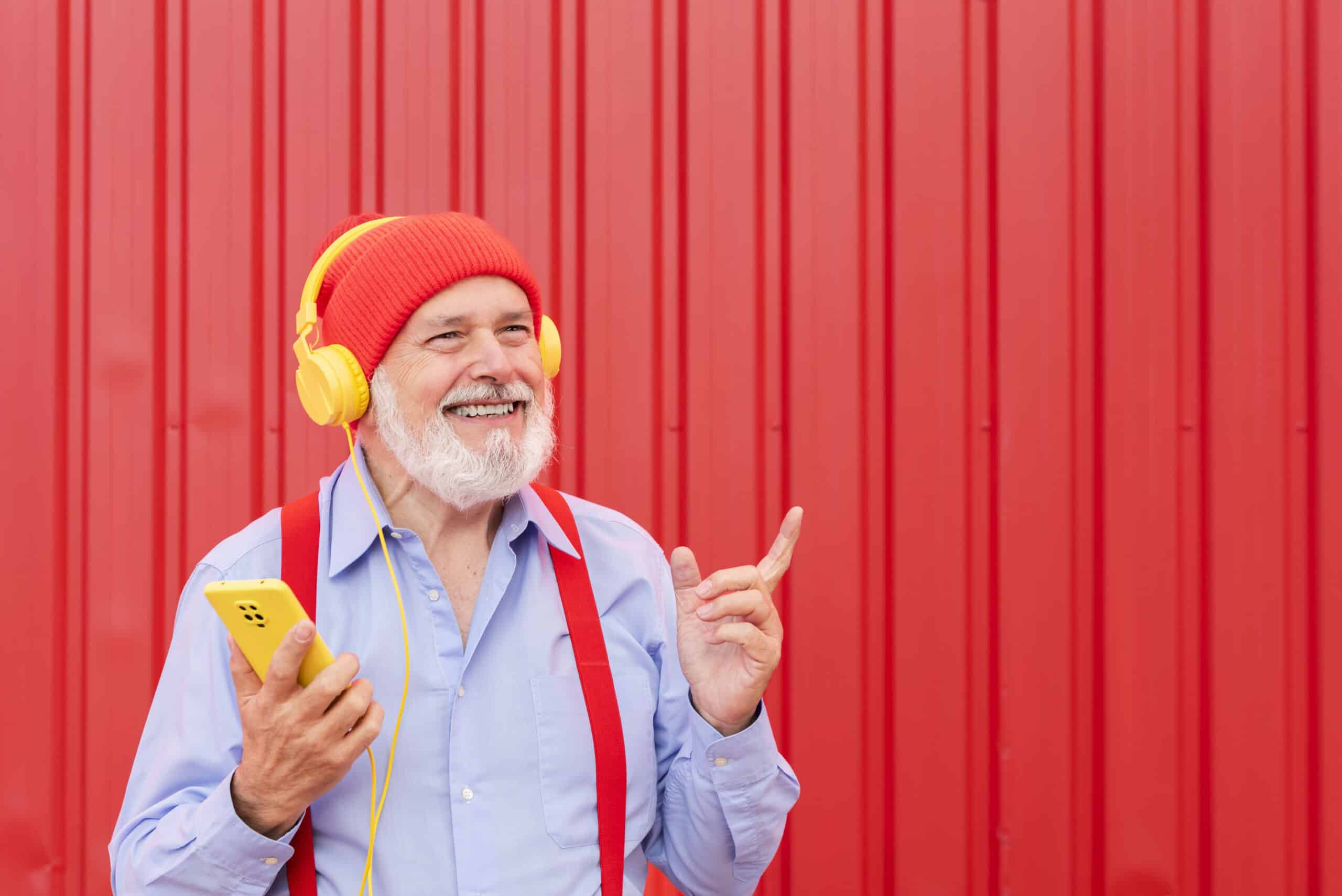 a modern pensioner listening to music with headphones on a red background