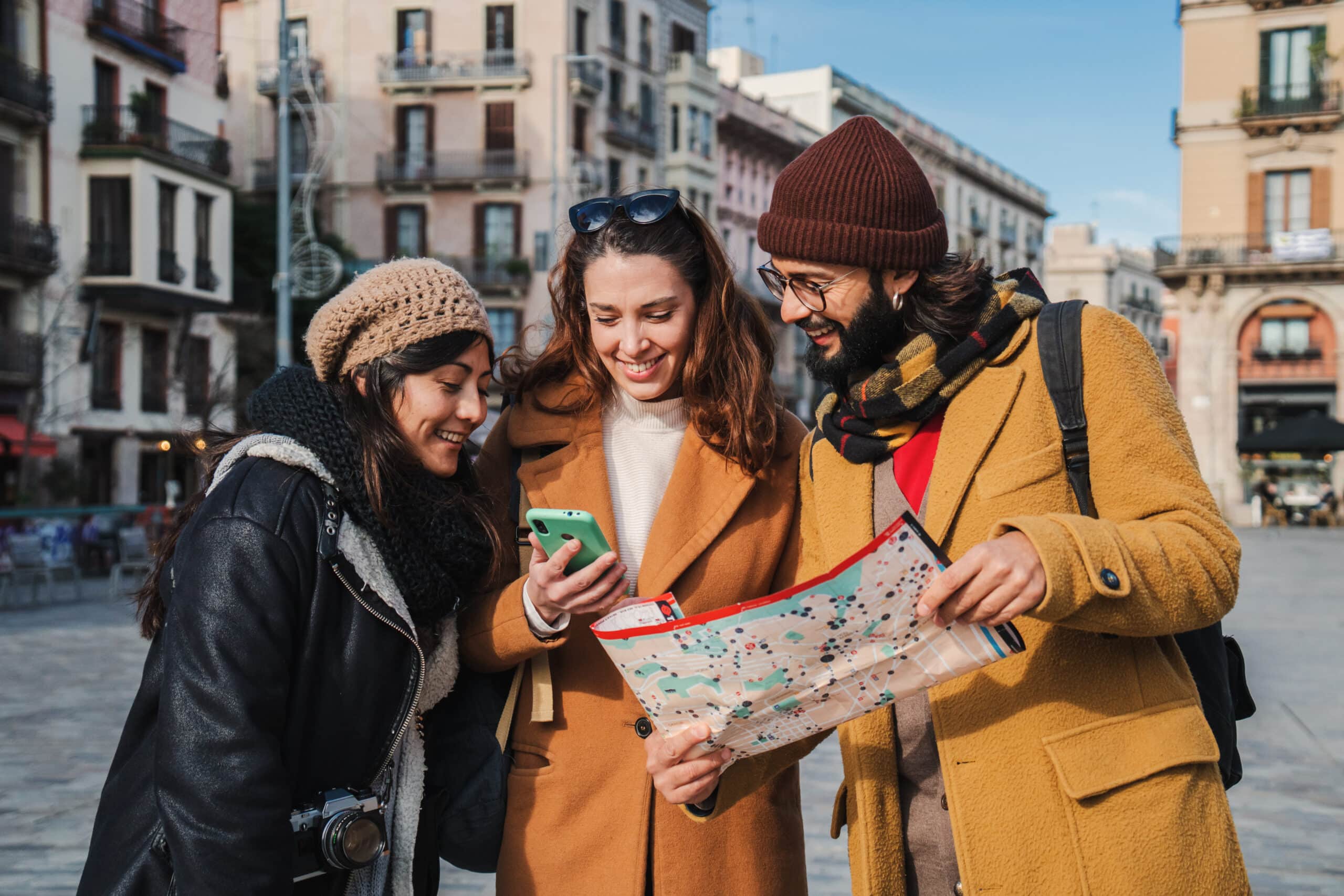 Group of tourist people sightseeing and searching a location on a map and on a smartphone app on a weekeand trip. Young travelers smiling looking together for directions on a guide visiting a city. High quality photo