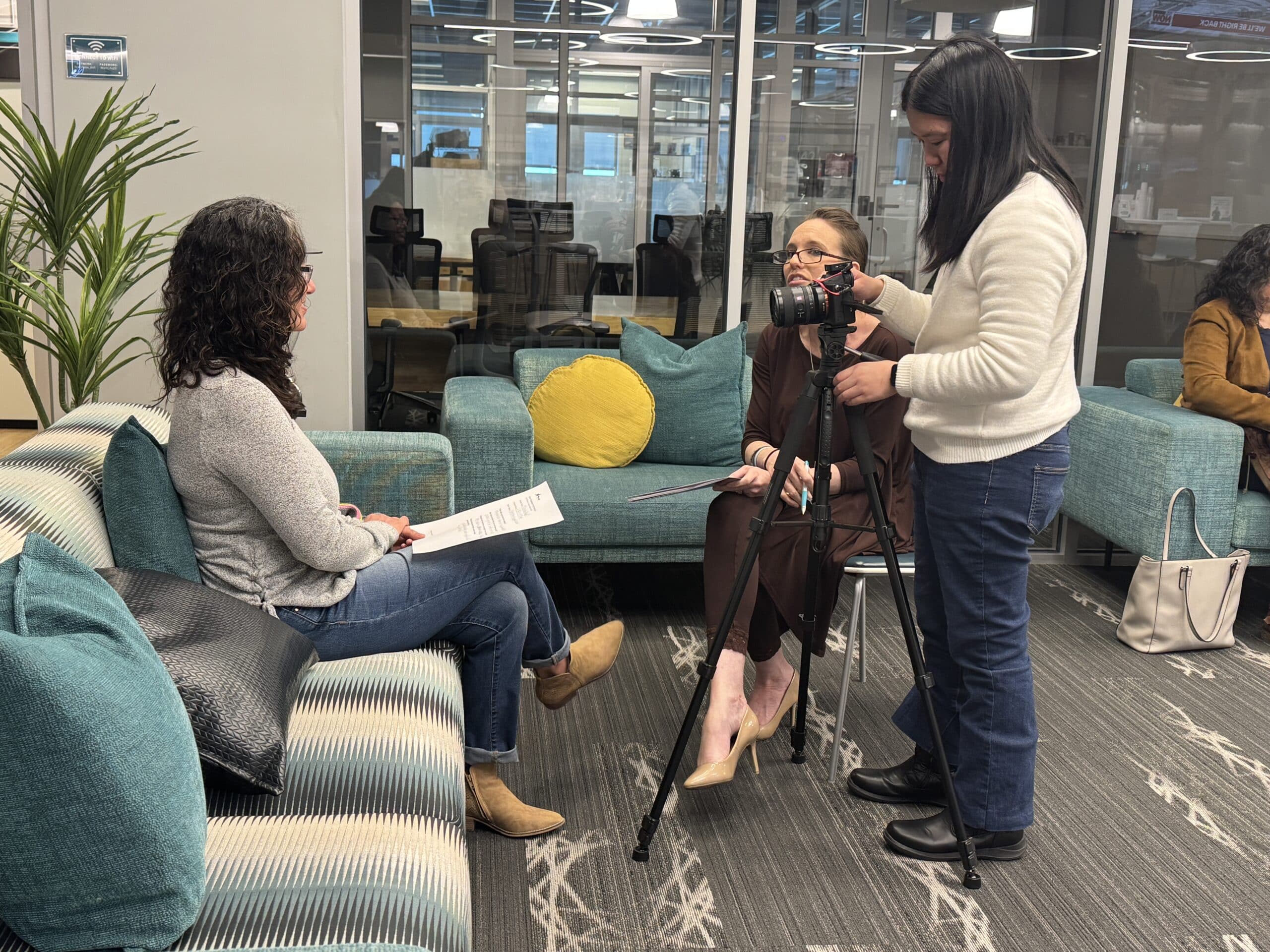 Three women preparing for a video interview in a modern office lounge