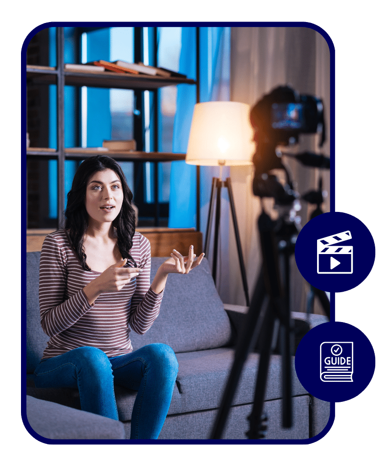 Woman sitting on a couch filming content with a camera and tripod, gesturing with her hands while explaining something, in a cozy living room setting.