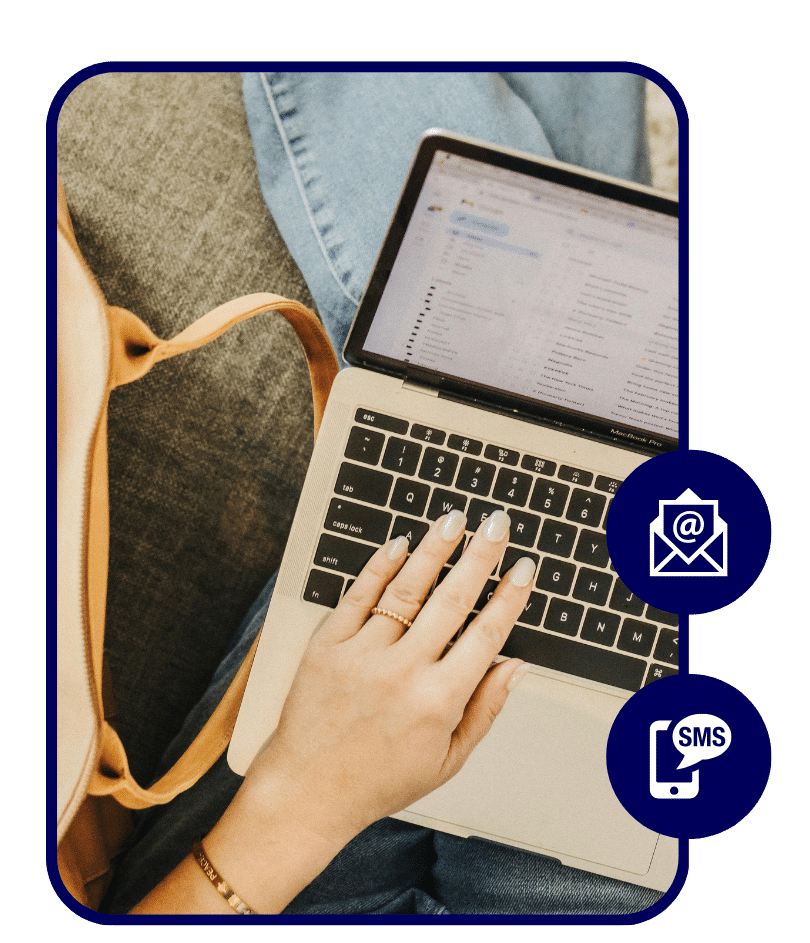 Close-up of a woman’s hand typing on a laptop showing an open email inbox, with a tan backpack beside her.